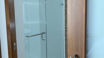 A modern bathroom with a glass shower enclosure, a wooden door, and a tiled floor.