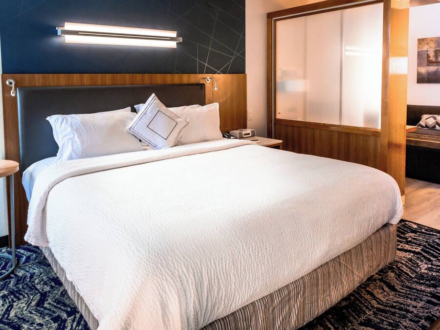 A neatly made bed with white bedding, a wooden headboard, and a bedside table with a lamp.