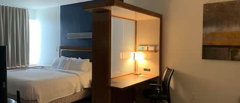 A hotel room with a bed, desk, chair, and a television.