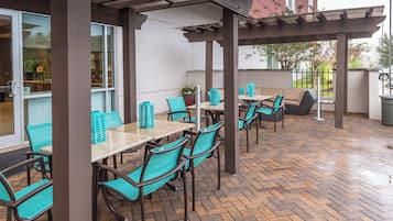 Un área de patio al aire libre con mesas y sillas, una pérgola y piso de ladrillo.