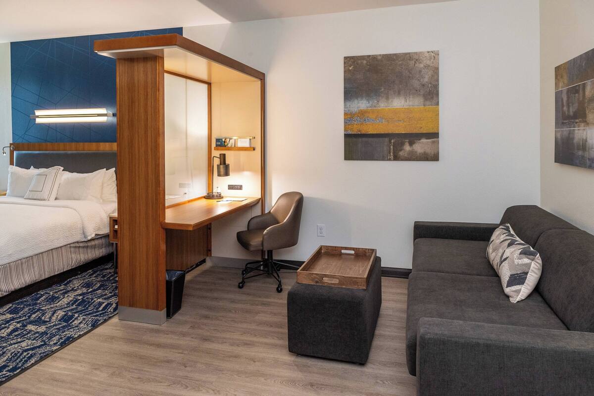 Una camera d'albergo moderna con un letto, una scrivania, una sedia, un divano e opere d'arte alle pareti.