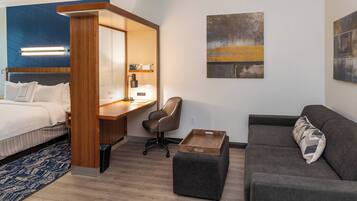 Una habitación de hotel moderna con cama, escritorio, sillón, sofá y obras de arte en las paredes.