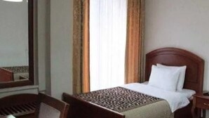 Ein Hotelzimmer mit Bett, Nachttisch, Stuhl, Lampe und einem Fenster mit Vorhängen.