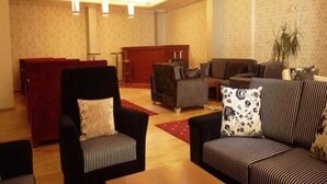 Eine Hotellobby mit Empfangstresen, Sitzgelegenheiten mit Sofas und Sesseln sowie Wandpapier mit Muster.