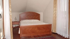 Ein Schlafzimmer mit einem hölzernen Bett, einem Nachttisch, einer Lampe und einem Fenster mit Vorhängen.