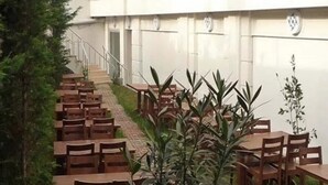 Ein Gebäude mit einer Treppe, die zu einer oberen Ebene führt, umgeben von Grünflächen und Außenbereichen mit Tischen und Stühlen.