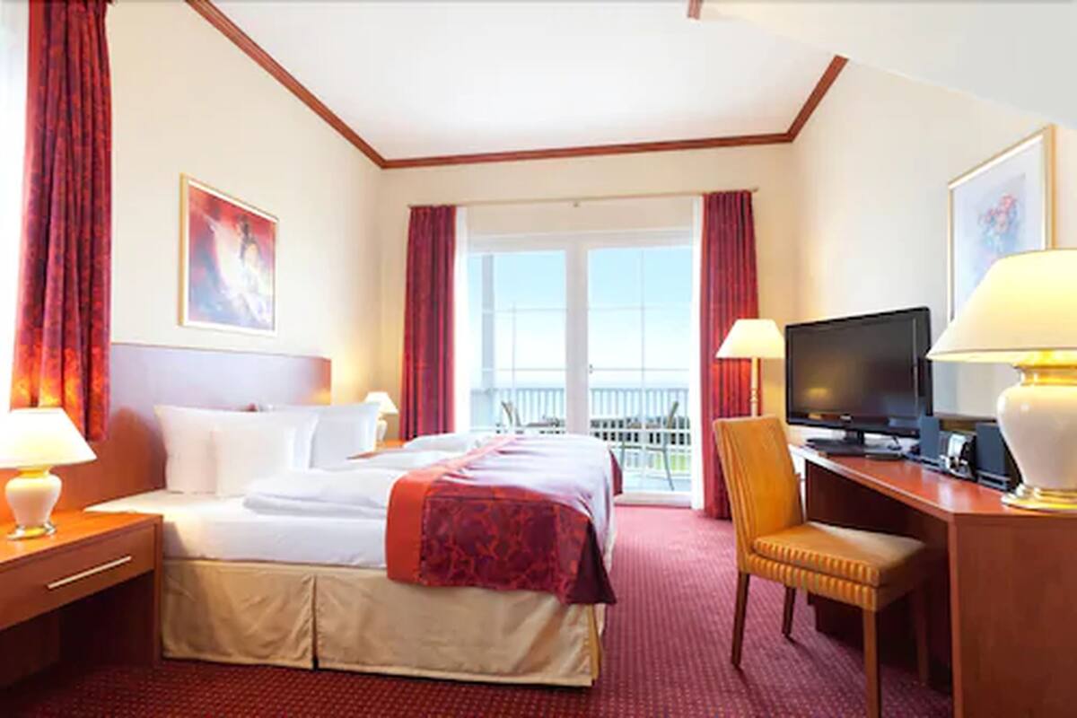Ein Hotelzimmer mit einem Bett, einem Schreibtisch mit Computer, einem Fernseher und einem Sessel.