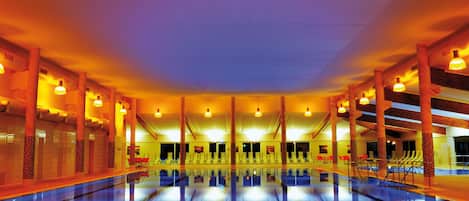 A large indoor swimming pool with multiple lanes, surrounded by seating areas and a high ceiling with exposed beams.