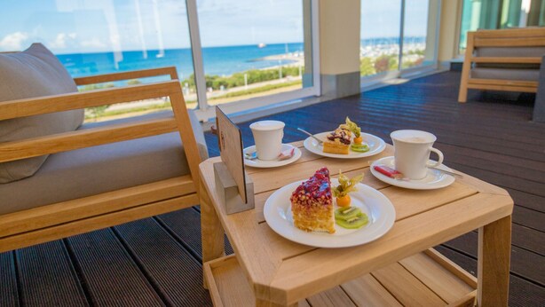 Um deck de madeira com uma mesa posta para dois, com vista para a praia e o oceano.