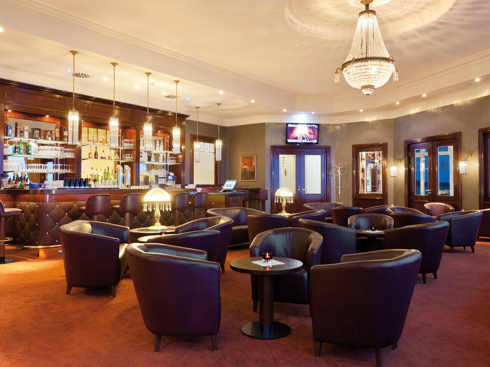 A bar area with leather seating, a television screen, and a chandelier.
