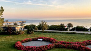 Um jardim com paisagismo, com um canteiro de flores circular, um banco e vista para o mar e um cais.