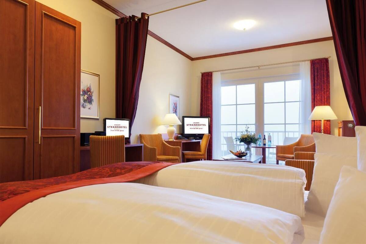 Ein Hotelzimmer mit zwei Betten, einem Schreibtisch mit Computer, einem Stuhl und einem Fenster mit Vorhängen.