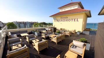 En takterrass på Morada Strandhotel med utomhusmöbler och utsikt över havet.