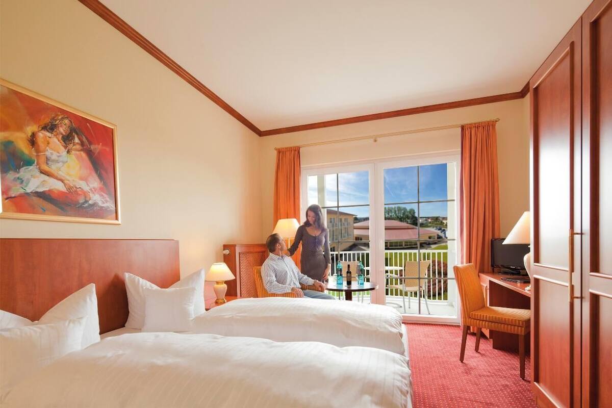 Ein Hotelzimmer mit einem großen Bett, einem Schreibtisch mit Stuhl, einem Fernseher und einem Balkon mit Aussicht.