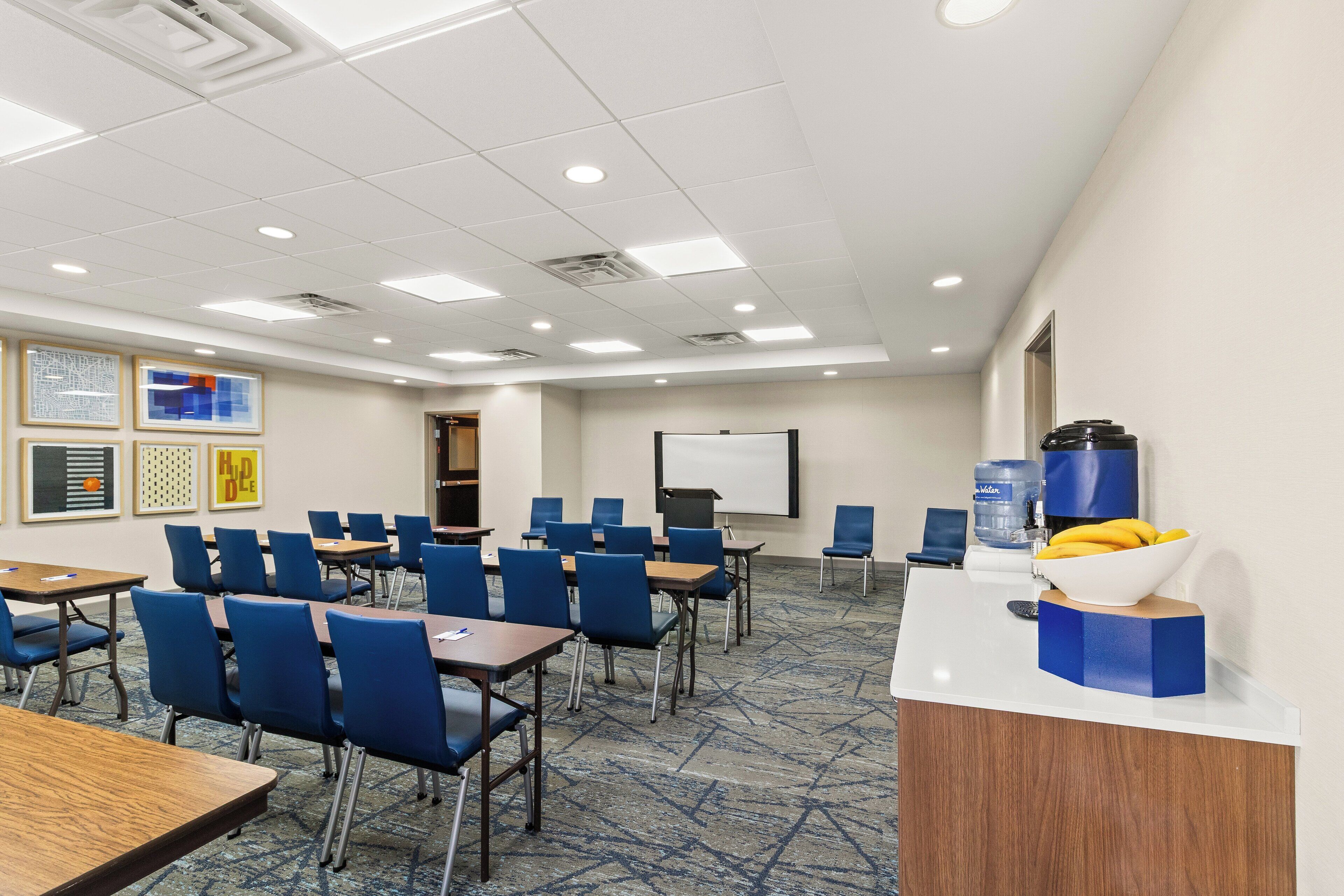 A conference room with tables and chairs, a whiteboard, and a water dispenser.