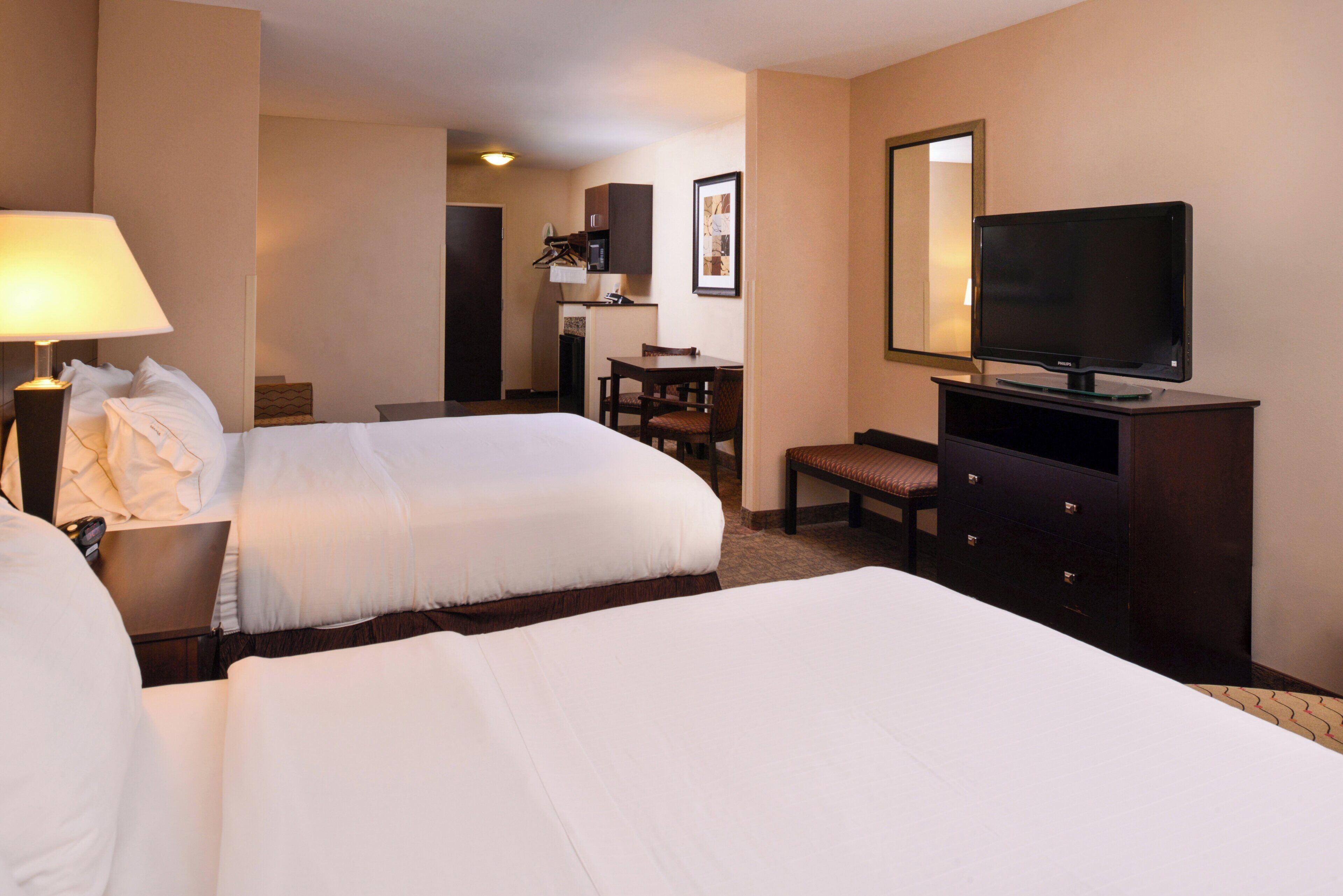 A hotel room with two beds, a desk, a chair, a television, and a mirror.