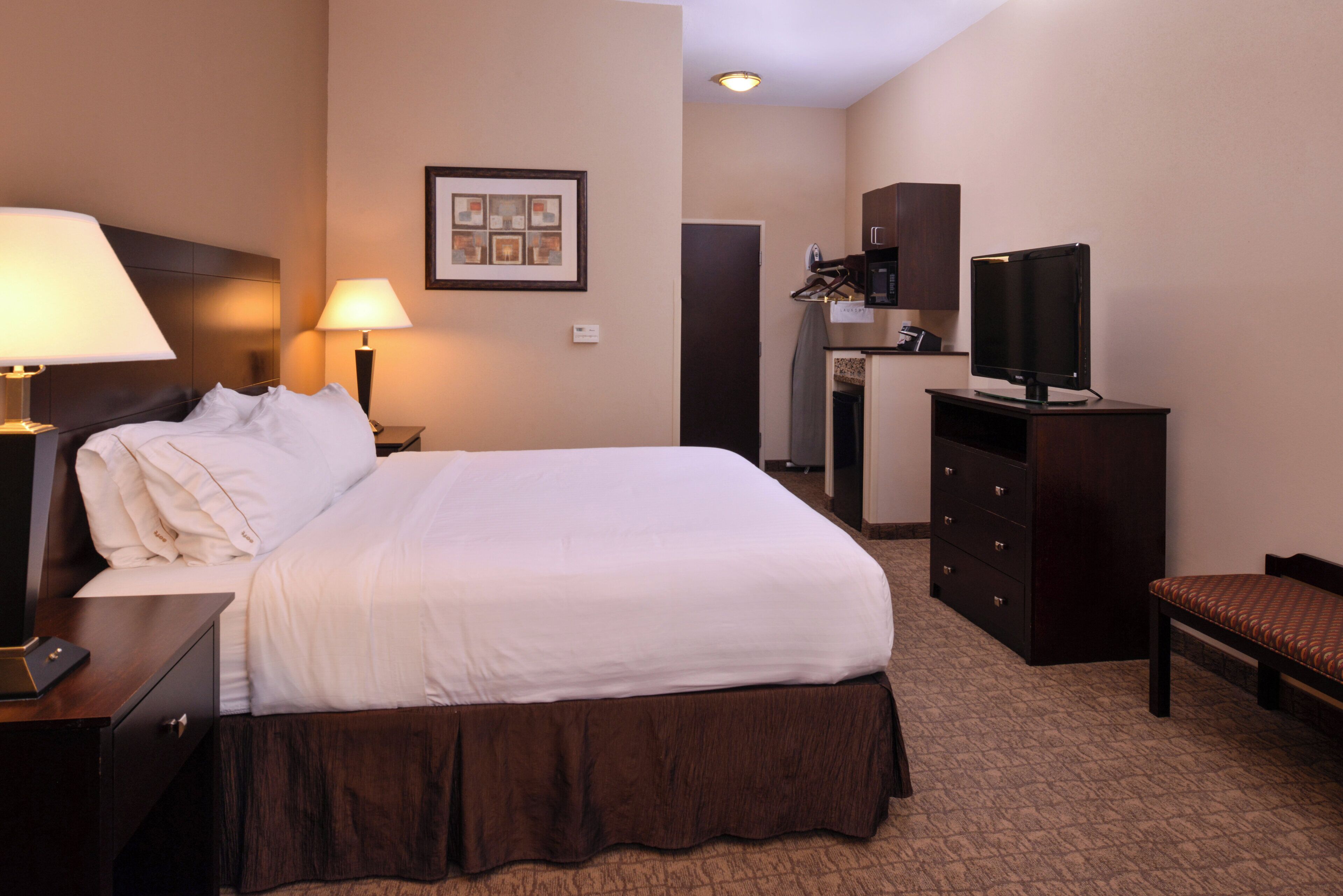 A hotel room with a bed, a desk, a dresser, a television, and a framed picture on the wall.