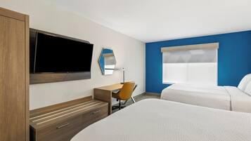Habitación de hotel con cama, escritorio, silla, televisor y ventana.