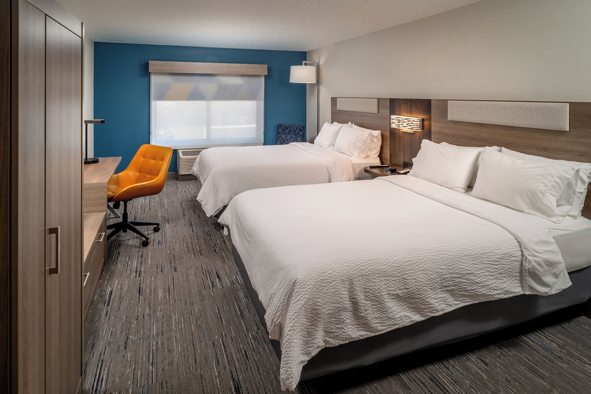 A hotel room with two beds, a desk, an orange chair, and a large window.