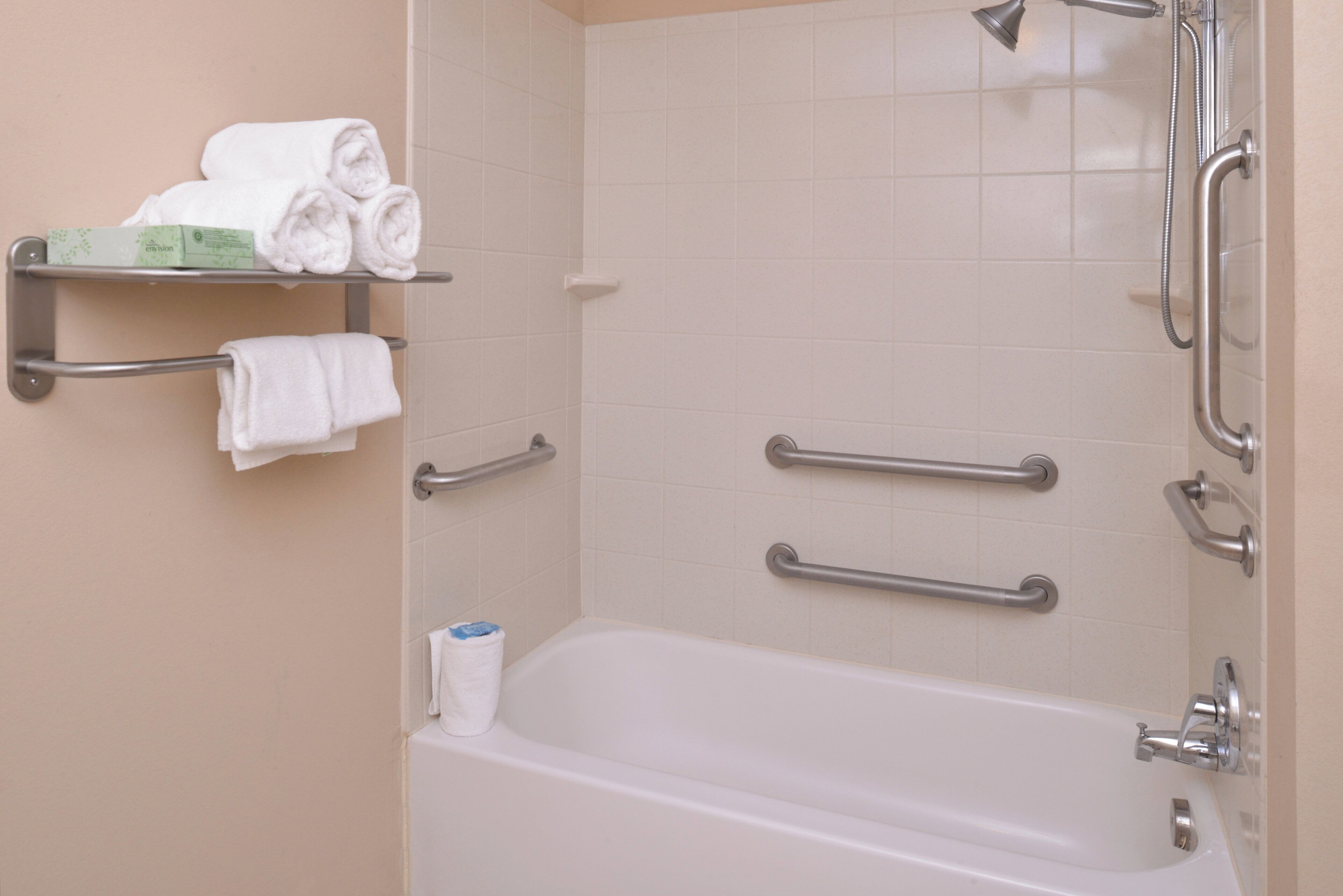 Ein Badezimmer mit einer Badewanne, einem Handtuchhalter mit gefalteten Handtüchern und Haltegriffen.