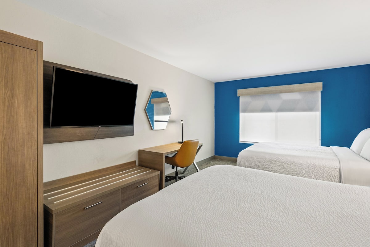 A hotel room with a bed, a desk, a chair, a TV, and a window.