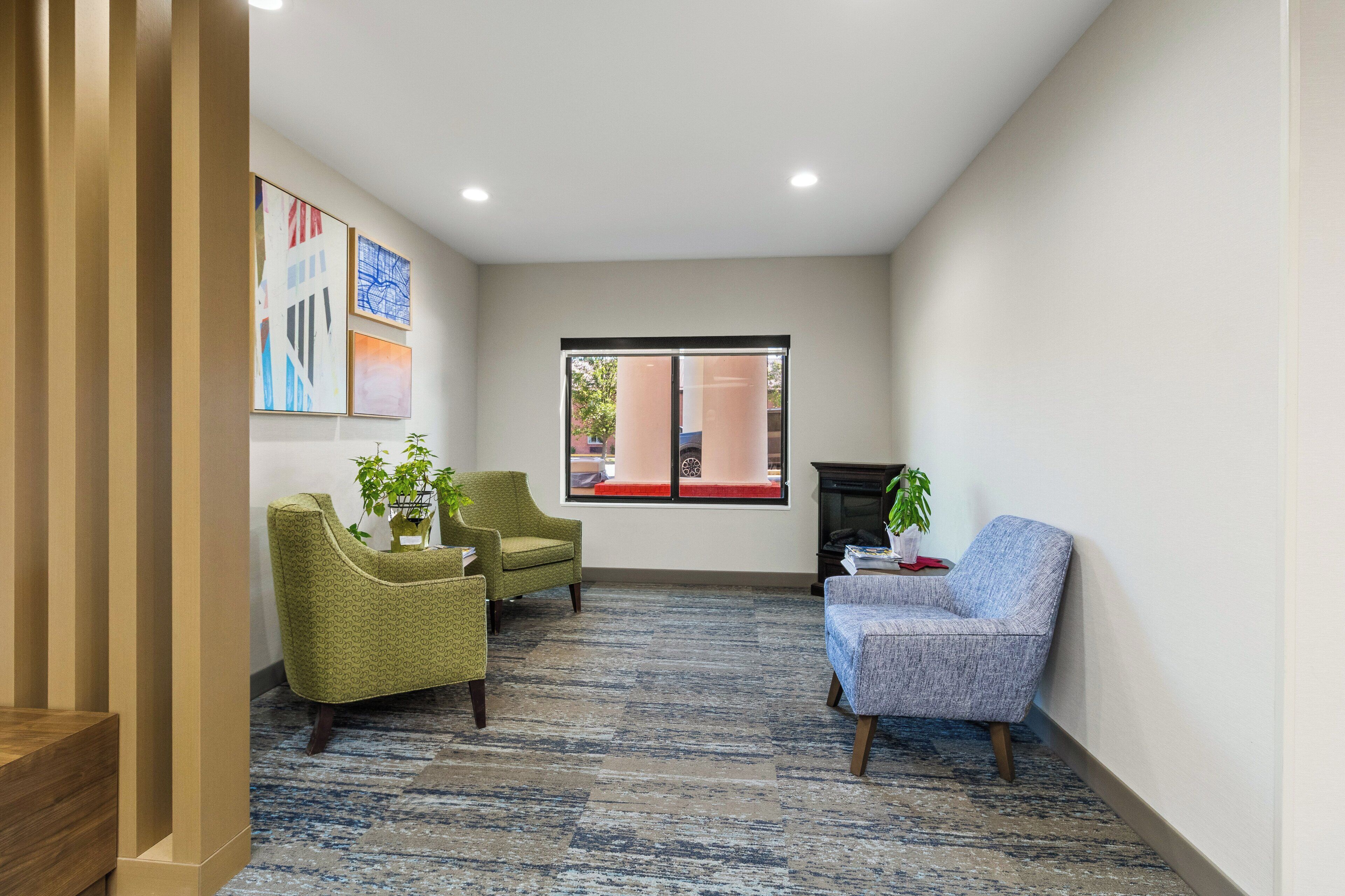 Een moderne lobby met een kamerbreed tapijt, twee fauteuils, een bank en een open haard.
