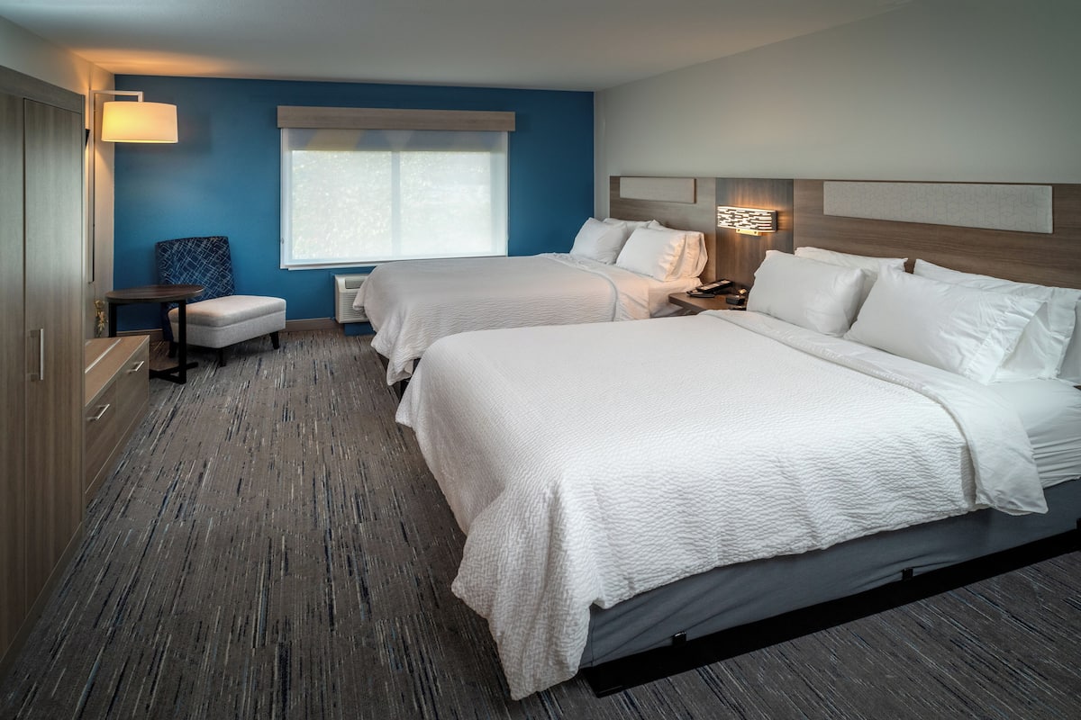 A hotel room with two beds, a desk, a chair, and a window.