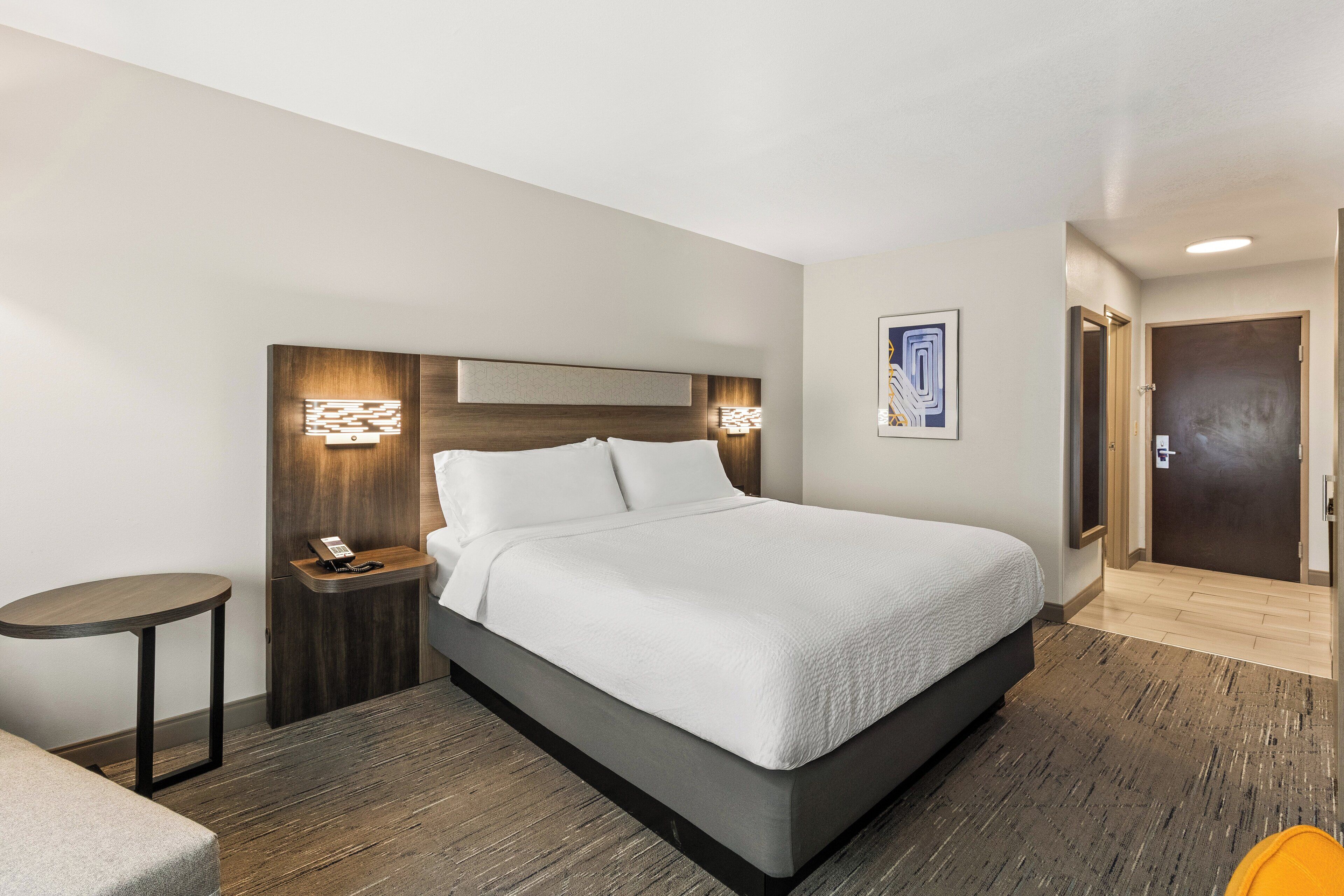 Una habitación de hotel moderna con una cama grande, una mesita de noche con teléfono y una pequeña mesa redonda.
