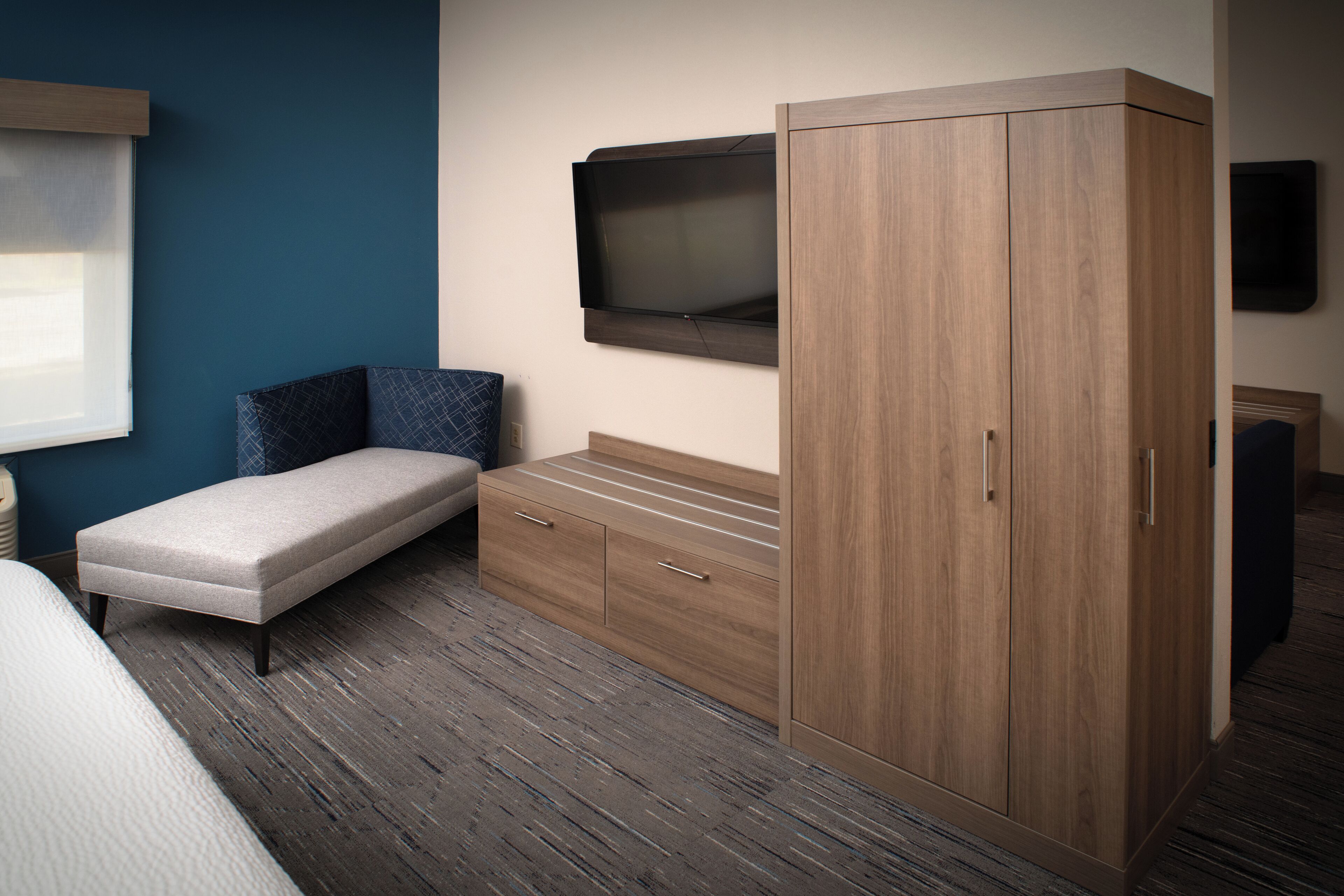 Ein Schlafzimmer mit Bett, einer Sitzbank, einem Kleiderschrank und einem Fernseher an der Wand.