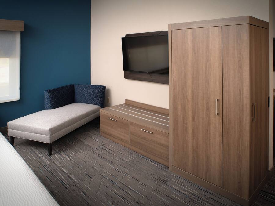 A bedroom with a bed, a bench, a wardrobe, and a television on the wall.