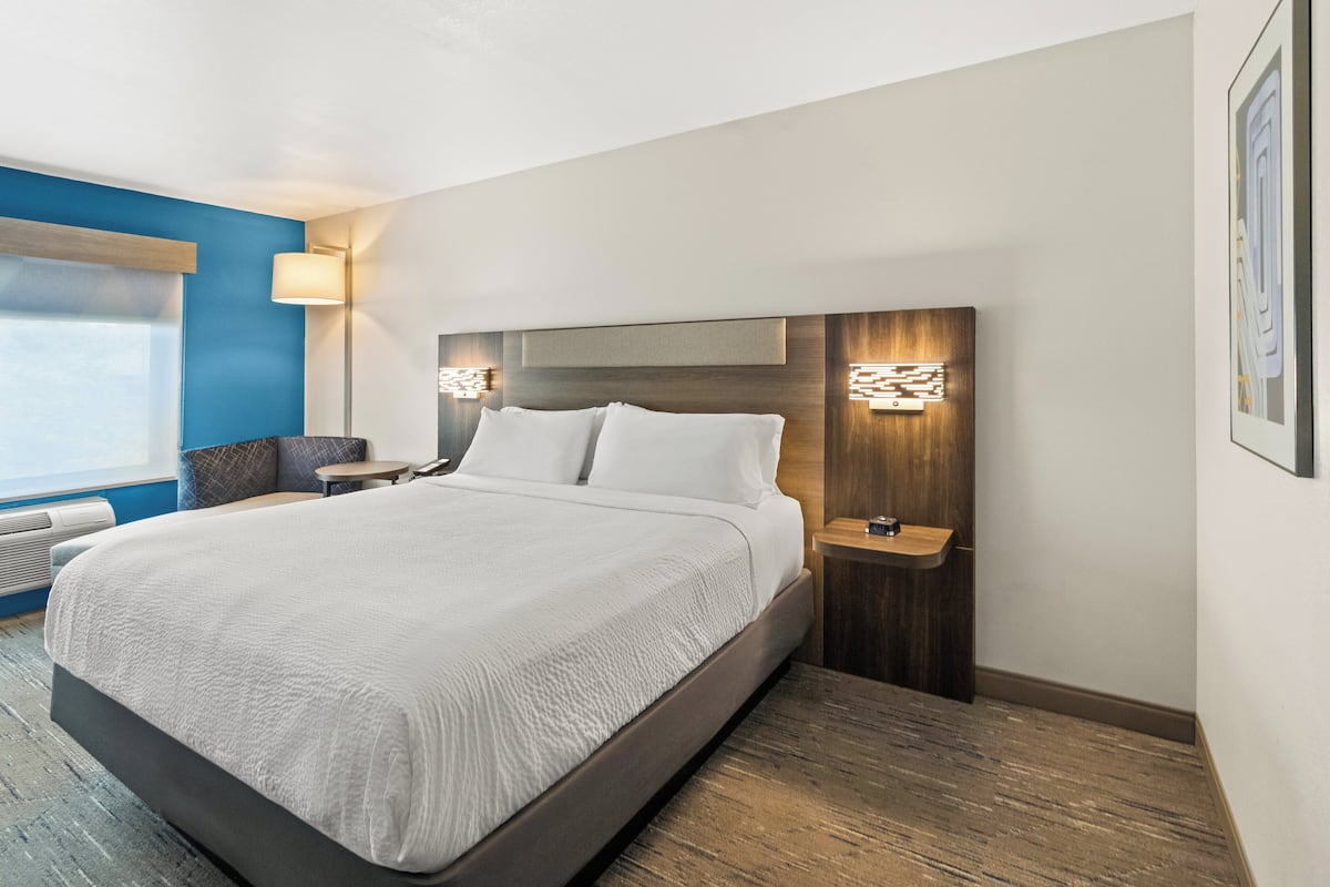 A modern hotel room with a large bed, bedside tables, a desk, and a window with blinds.