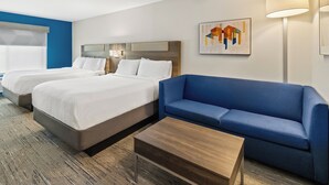 A hotel room with two beds, a blue sofa, a wooden coffee table, and a lamp. - Holiday Inn Express and Suites Fairmont by IHG (Fairmont)