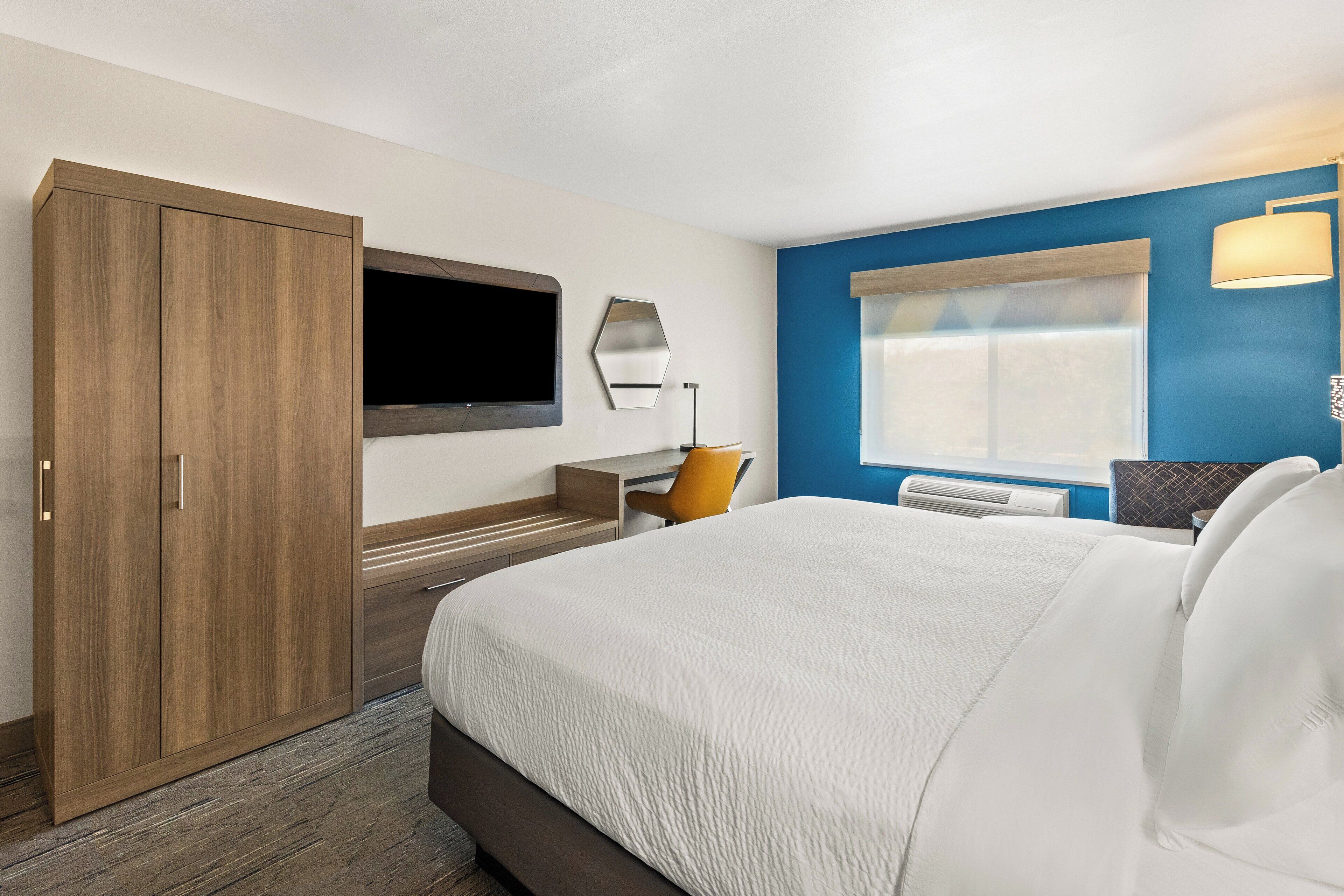 Camera d'albergo con un letto grande, un armadio in legno, una scrivania con una sedia, una TV a schermo piatto montata a parete e una finestra con vista.