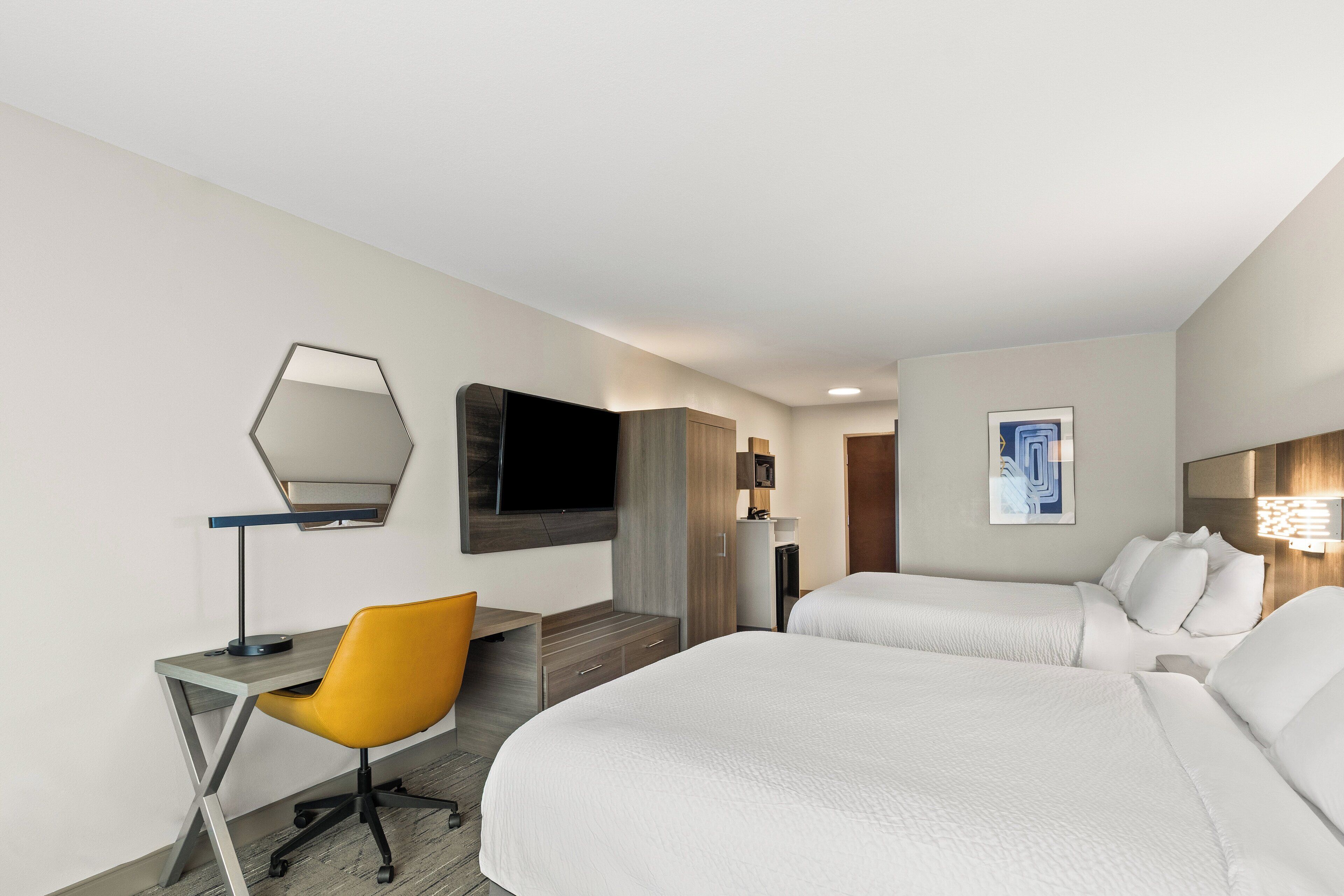 Ein Hotelzimmer mit zwei Betten, einem Schreibtisch mit Stuhl, einem Fernseher und einem Bild an der Wand.