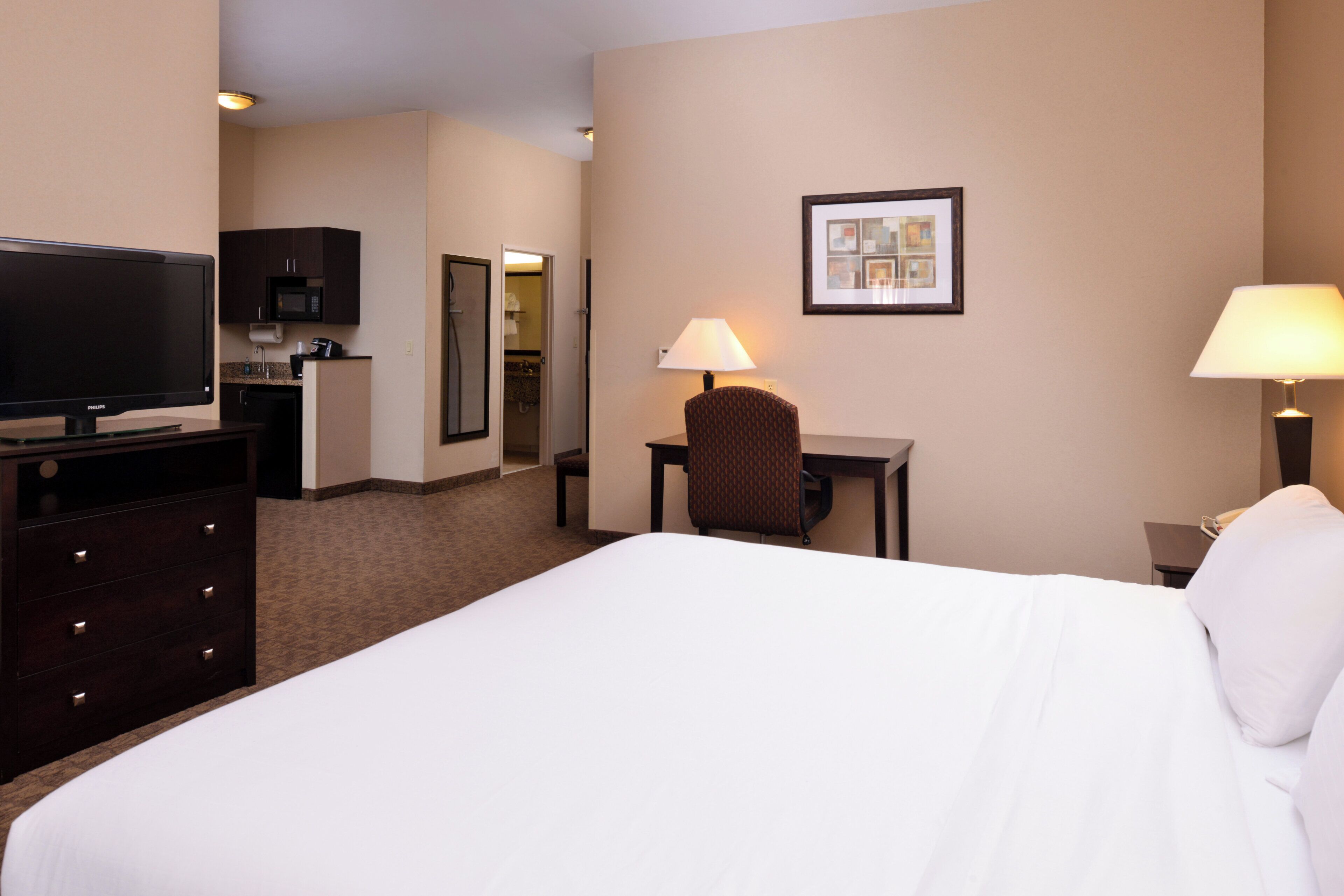 A hotel room with a bed, a desk with a chair, a television, a microwave, and a framed picture on the wall.