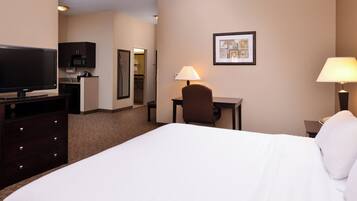 A hotel room with a bed, a desk with a chair, a television, a microwave, and a framed picture on the wall.