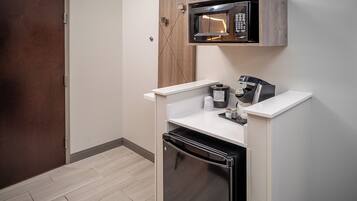 Una kitchenette compacta con microondas, cafetera y refrigerador.