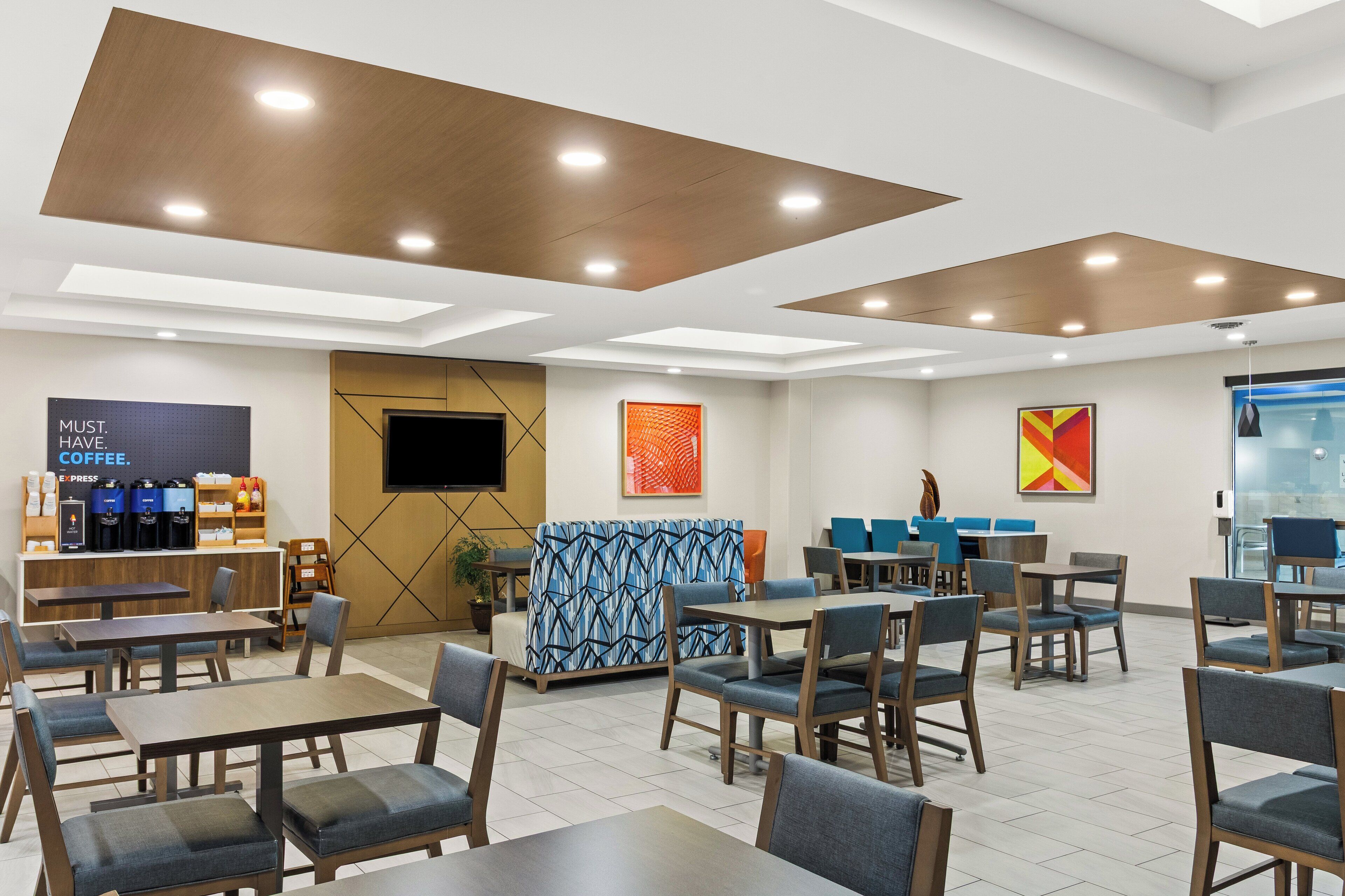 A modern cafe with multiple seating areas, a coffee station, and artwork on the walls.