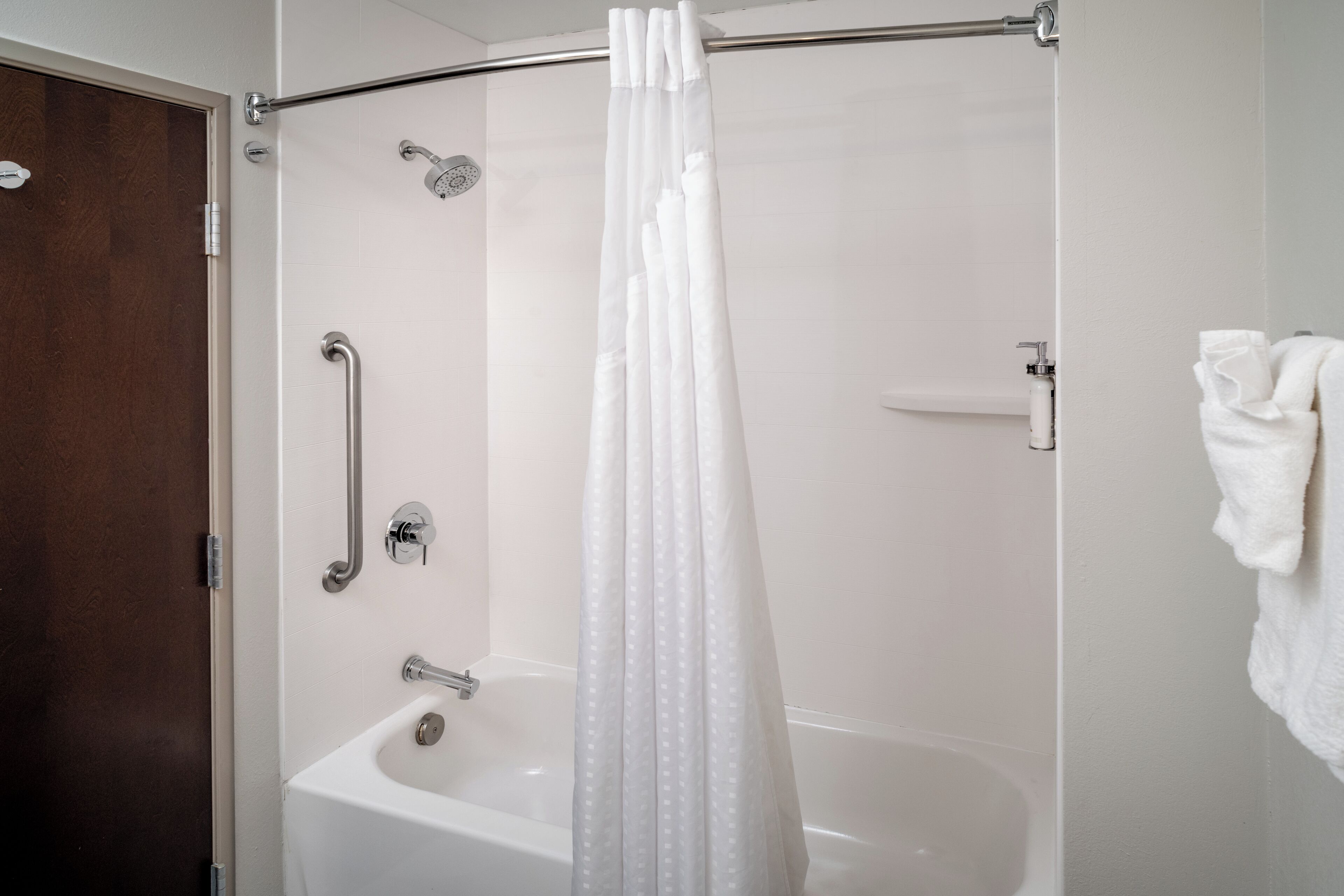 Une salle de bain moderne dotée d’une douche à l’italienne, de barres d’appui et d’une baignoire blanche.
