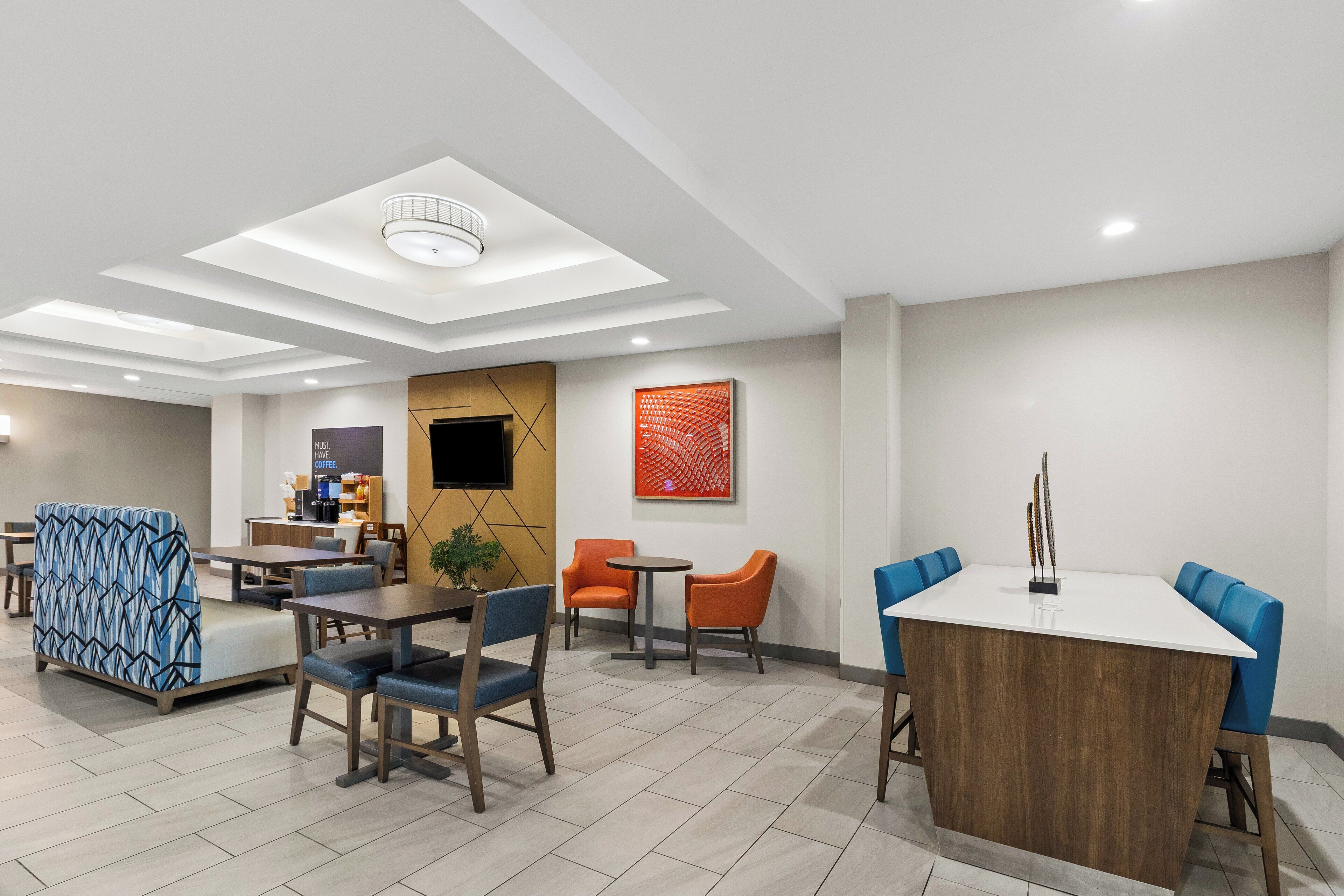 Eine moderne Hotelhalle mit einer zentralen Sitzecke, einer Kaffeestation und einem großen Bildschirm.