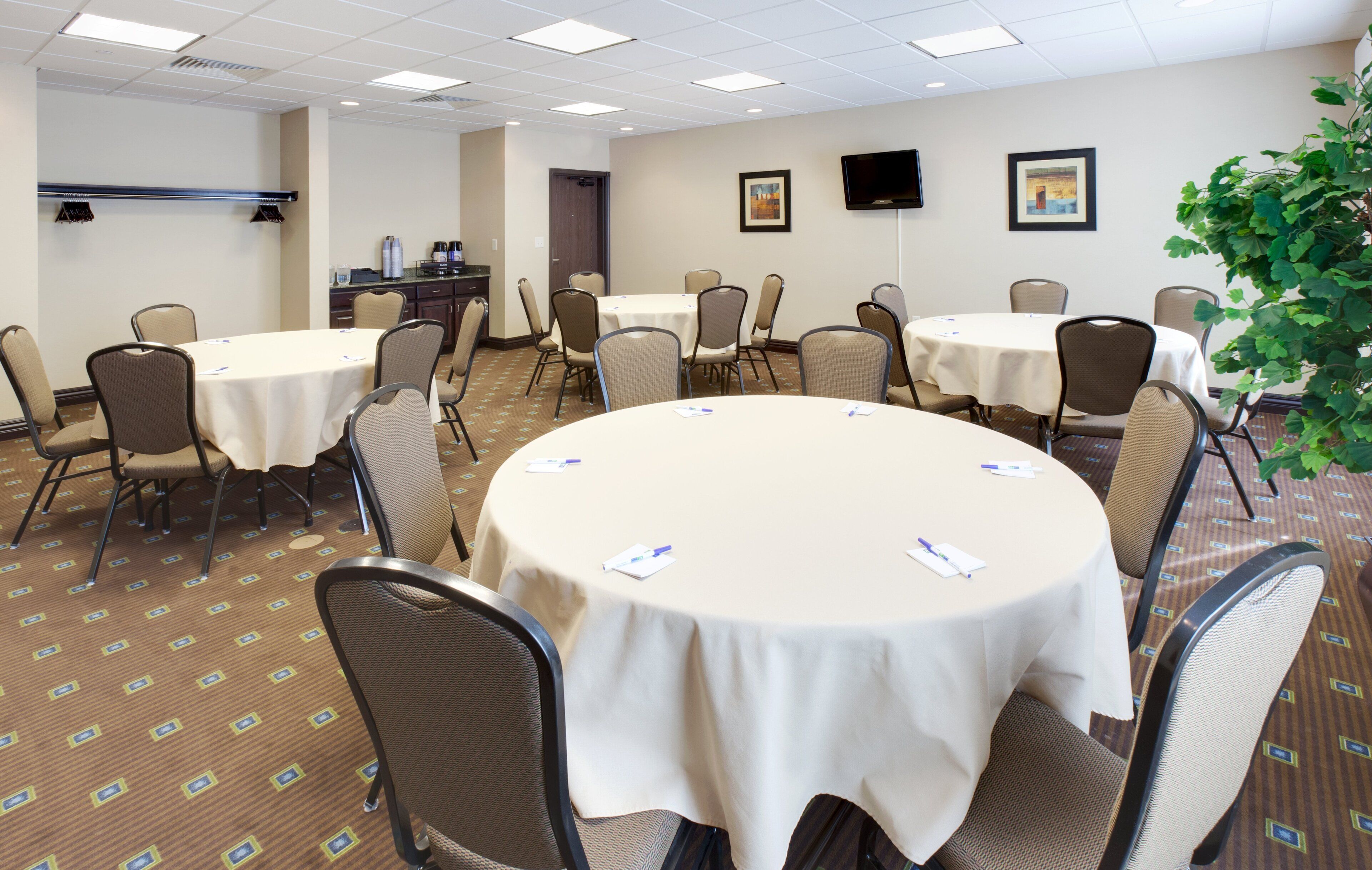 A conference room with round tables, chairs, and a television on the wall.
