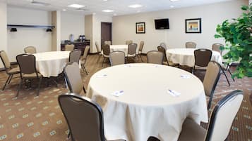 A conference room with round tables, chairs, and a television on the wall.