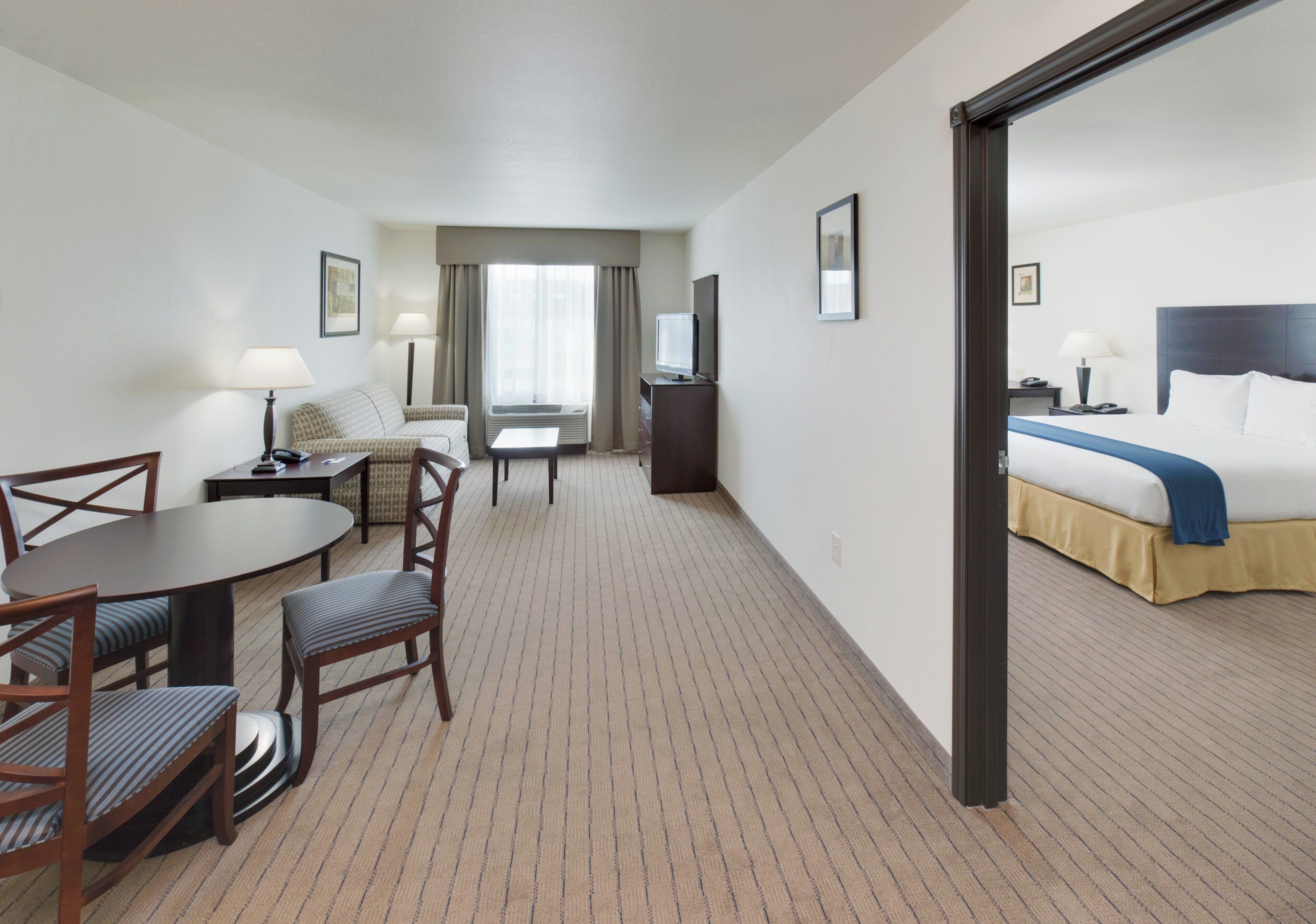 Habitación de hotel con cama, escritorio con silla, televisor y ventana con cortinas.