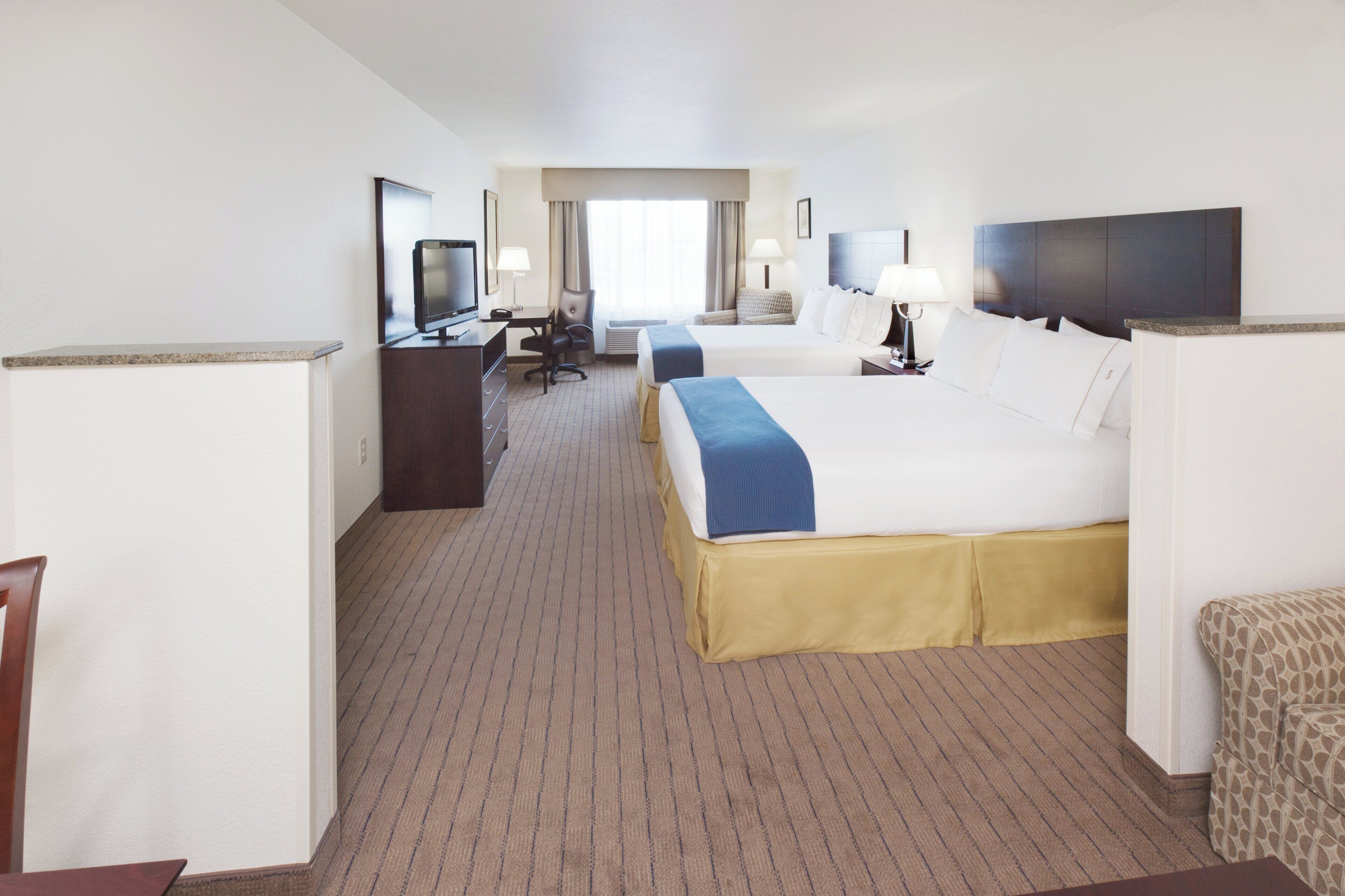 A hotel room with two beds, a desk, a television, and a chair.