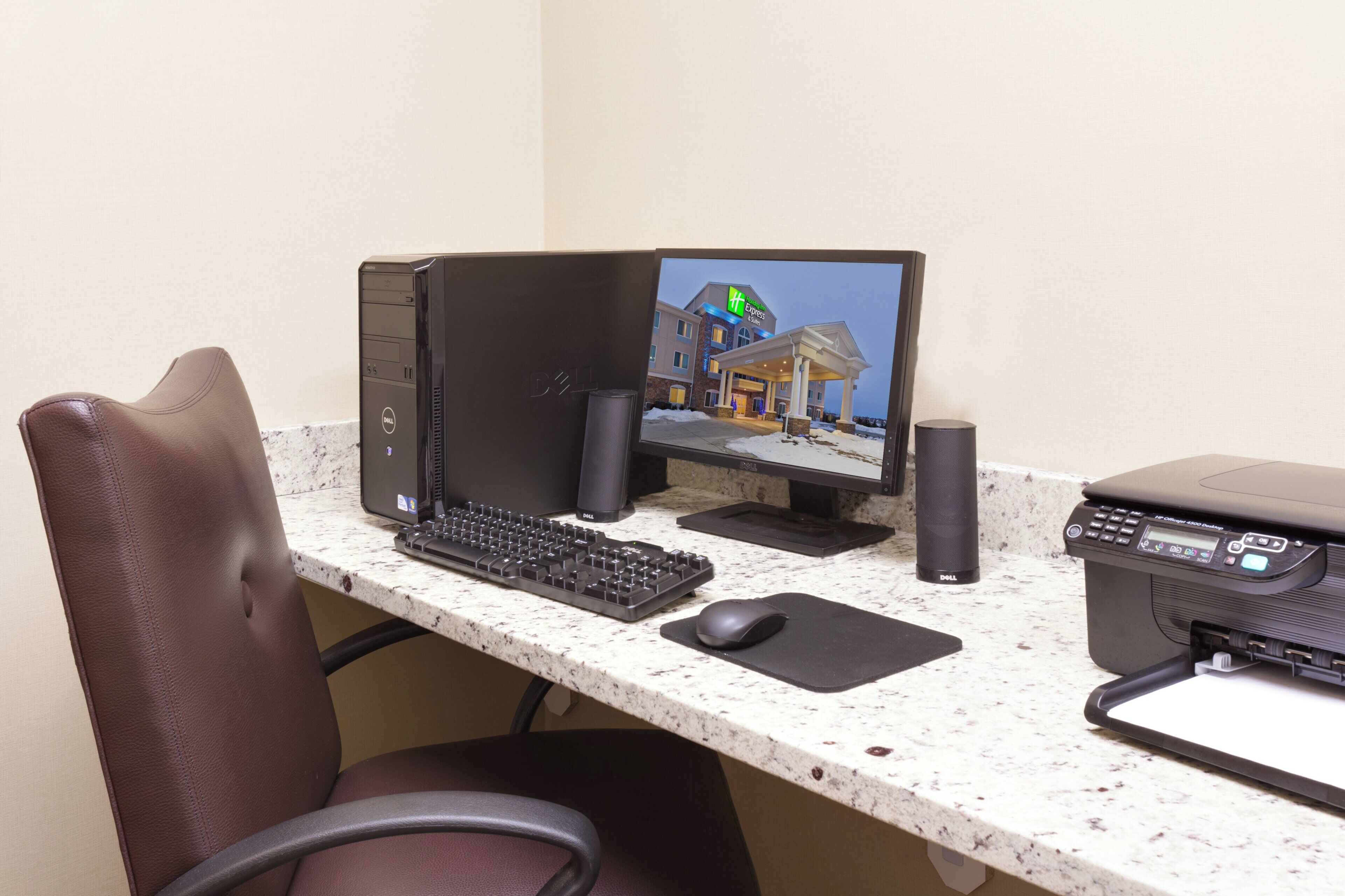 A hotel room with a desktop computer, a printer, and a chair.