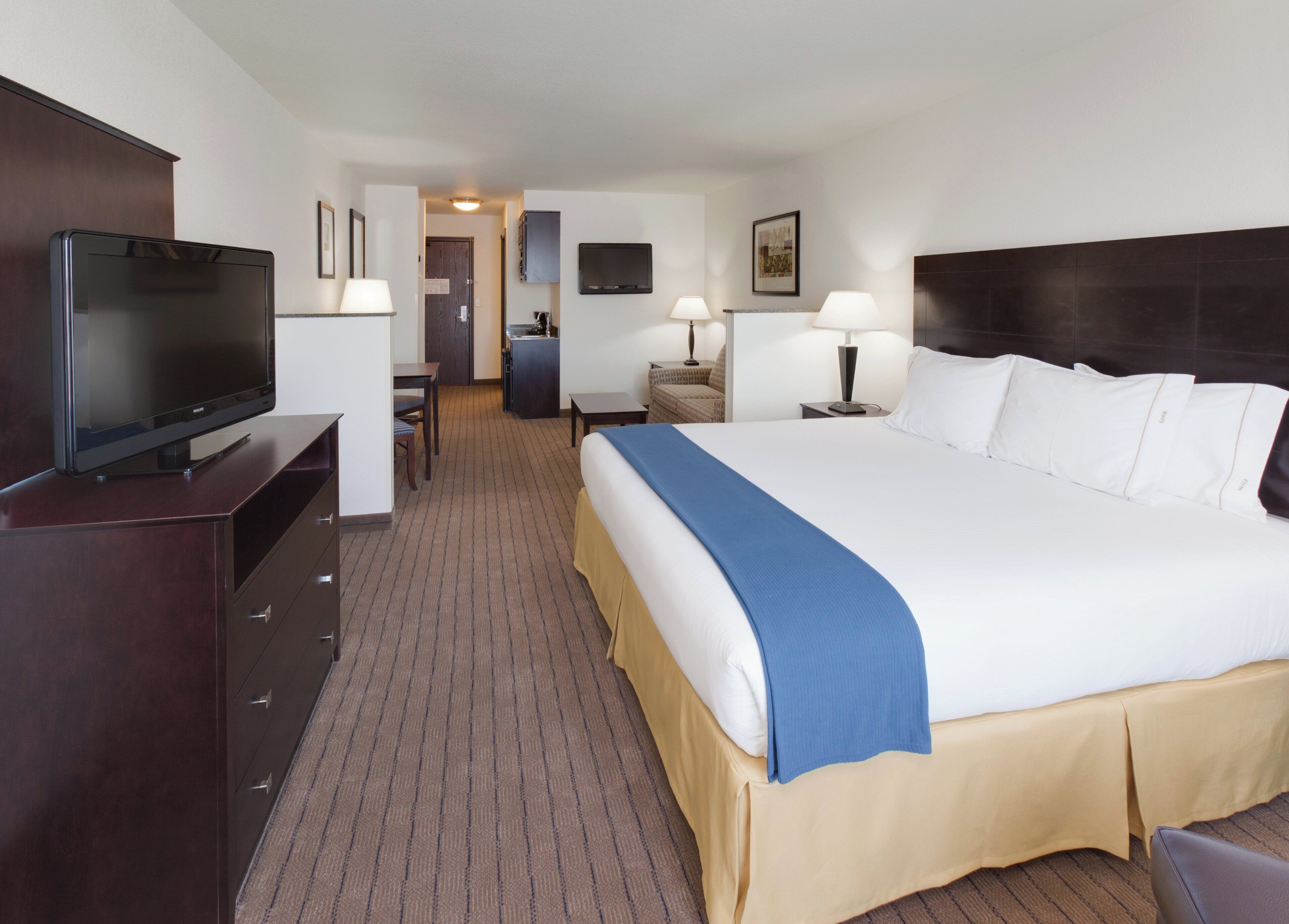 Une chambre d’hôtel avec un grand lit, une télévision, un bureau avec une chaise et une kitchenette.