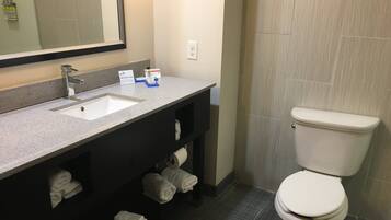 Un baño con lavamanos, espejo, toallero y retrete.