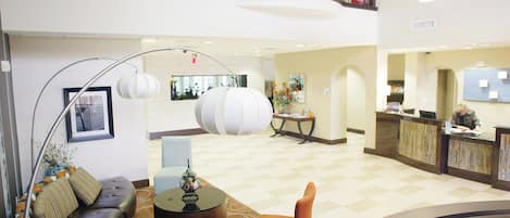 Eine Hotelhalle mit Rezeption, einer Sitzecke inklusive Sofa und Sesseln, einer Dekovase und einer großen Stehlampe.