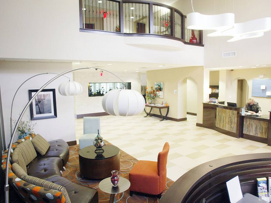A hotel lobby with a reception desk, seating area with a sofa and chairs, a decorative vase, and a large floor lamp.