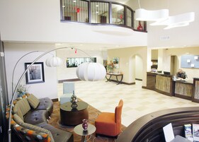 Un hall de hotel con una recepción, zona de estar con un sofá y sillas, un jarrón decorativo y una lámpara de pie grande.